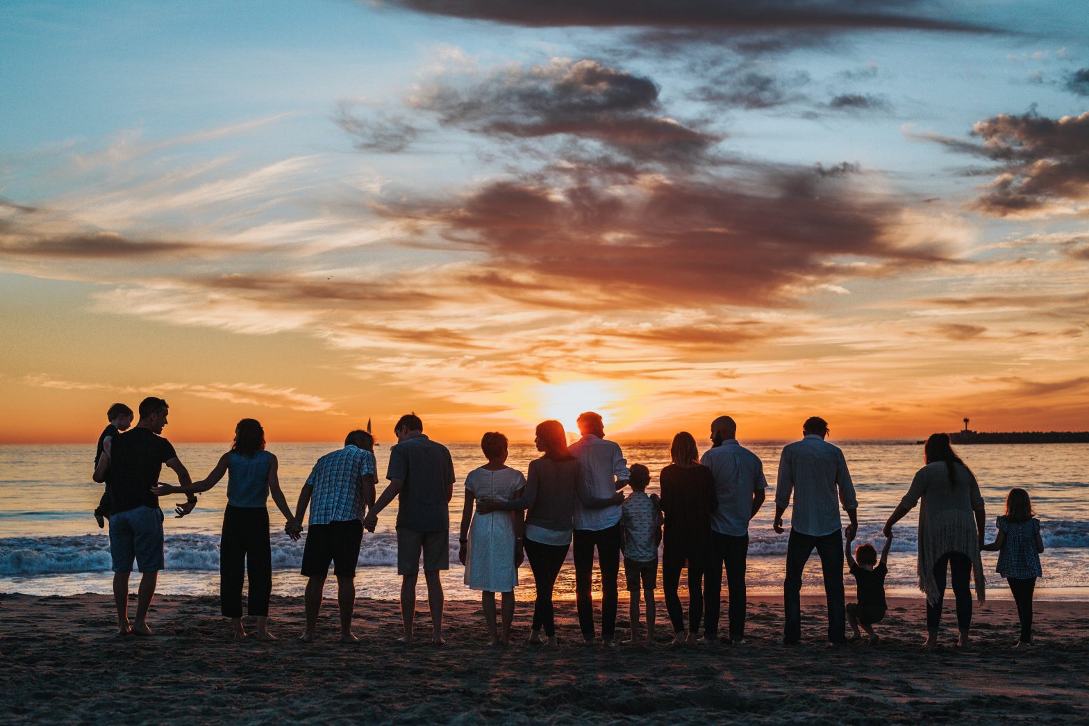 People standing together on a beach enjoying the sunset.